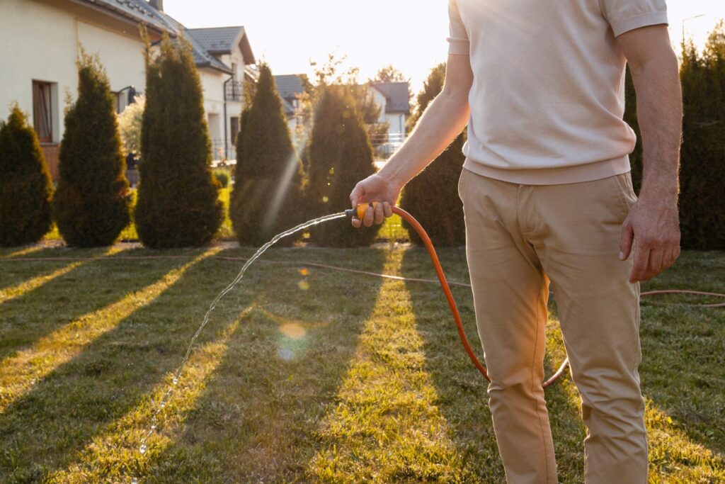 Florida homeowner watering a residential lawn with a garden hose to promote healthy grass growth and maintain a lush landscape.